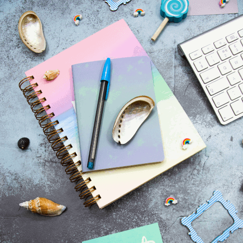 rainbow-notepad-flatlay-shells-mac-keyboard-pens-on-a-shiny-dark-background